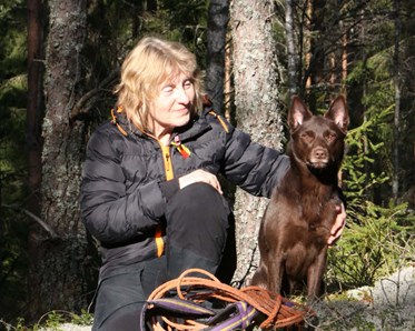 Ann-Sofie Lindgren sitter i en solig glänta med sin bruna kelpie och de har precis gått ett spår.