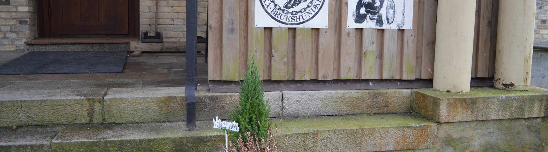 Bild på klubbstugans entre med en blomkruka med en välkommenskylt,