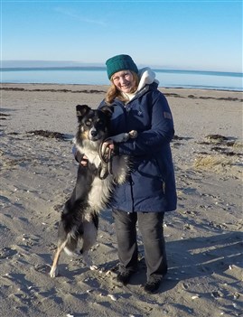 Sofie Liahaugen som står på stranden med sin hund i famnen.