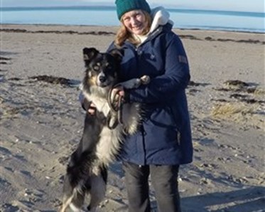 Sofie Liahaugen som står på stranden med sin hund i famnen.