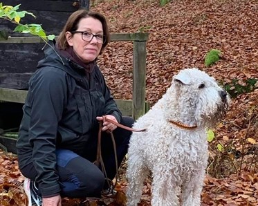 Vår instruktör Estelle Palmquist i svart jacka sitter på huk bland bruna höstlöv intill sin wheatenterrier.