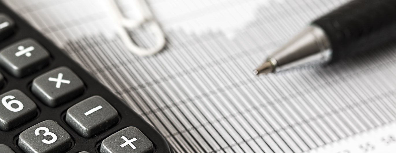 Svartvit bild som visar kalkylator och beräkning, penna, papper och gem.