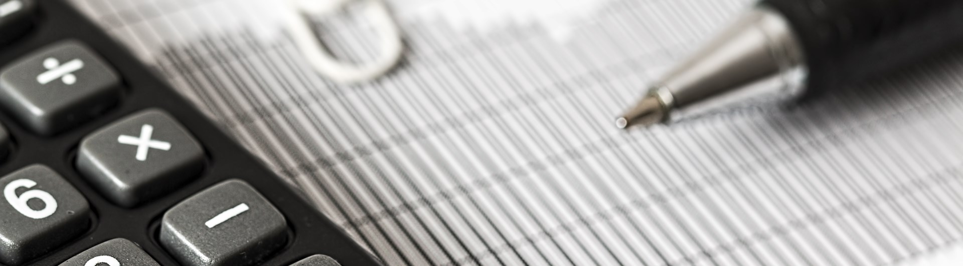 Svartvit bild som visar kalkylator och beräkning, penna, papper och gem.