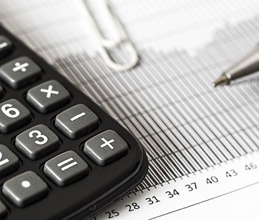 Svartvit bild som visar kalkylator och beräkning, penna, papper och gem.