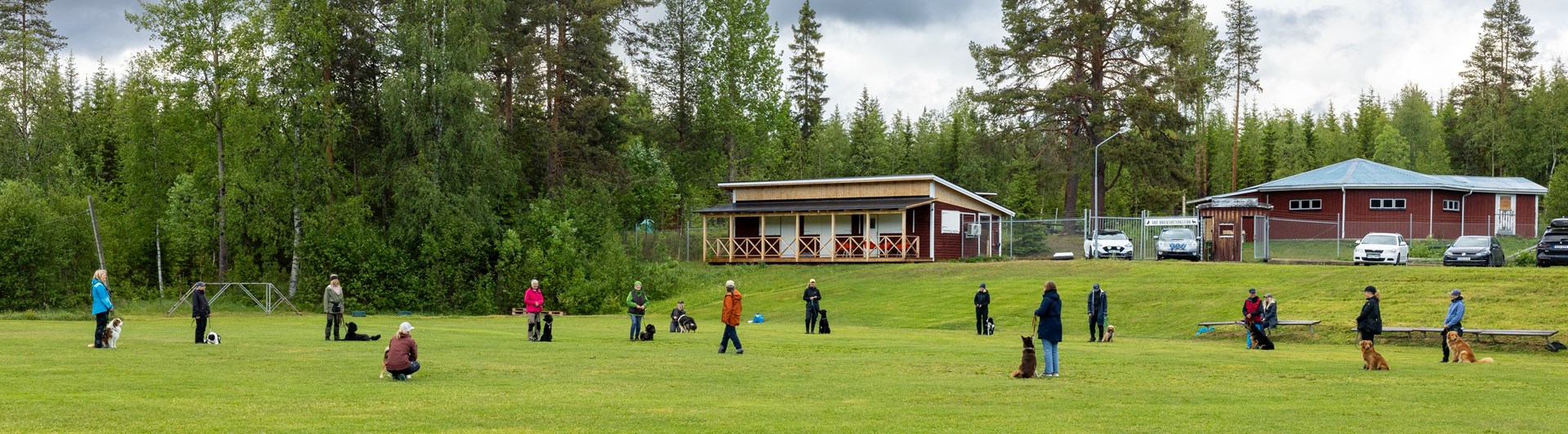 Klubbstugan. Folk tränar med sina hundar framför stugan.