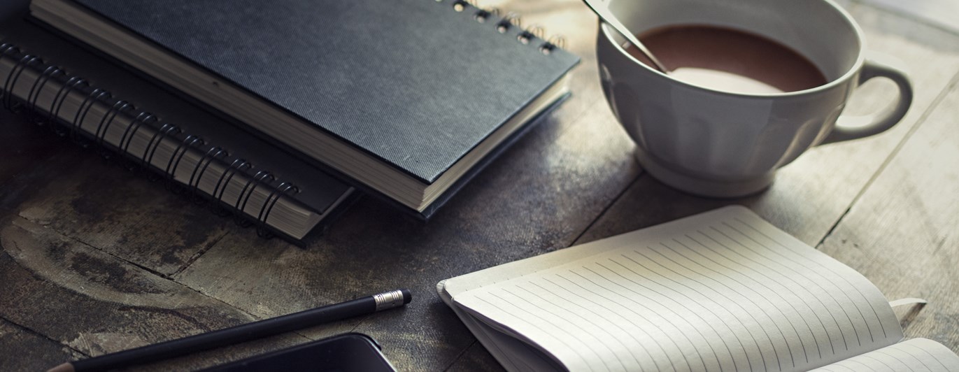 Bild som visar administration på ett bord med ipad, kaffemugg, skrivblock och penna.