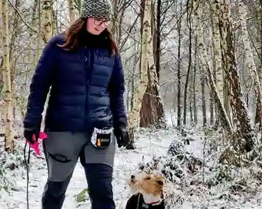 En ung kvinna och hennes hund går i en vintrig skog.