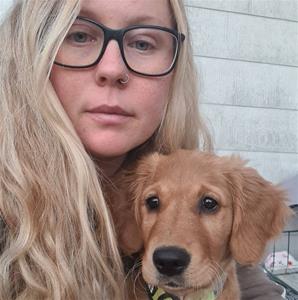 Kvinna med långt blont hår med svarta glasögon som har en golden retriever valp i famnen