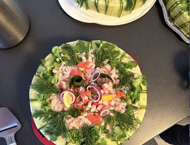 En bild ovanifrån på två runda smötgåstårtor garnerade med gurka, räkor, dill, citron, stenbitsrom och purjolök.