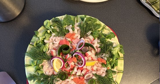 En bild ovanifrån på två runda smötgåstårtor garnerade med gurka, räkor, dill, citron, stenbitsrom och purjolök.