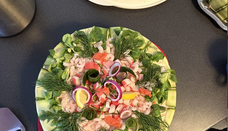 En bild ovanifrån på två runda smötgåstårtor garnerade med gurka, räkor, dill, citron, stenbitsrom och purjolök.