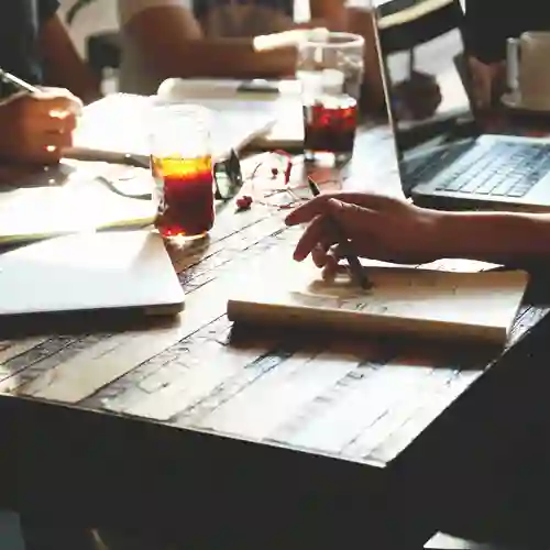 Bild på mötesbord med pennor, block, dator och skrivande händer.