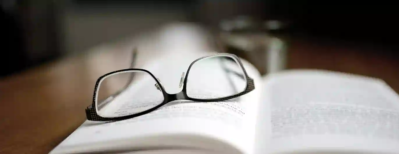 Bild som visar ett par glasögon som ligger på en uppslagen bok.