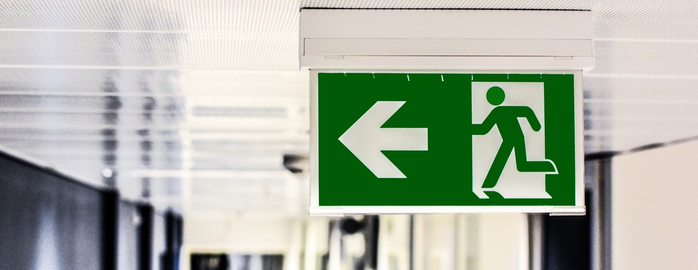 Bild på en skylt som visar en nödutgångsskylt i taket på en korridor.