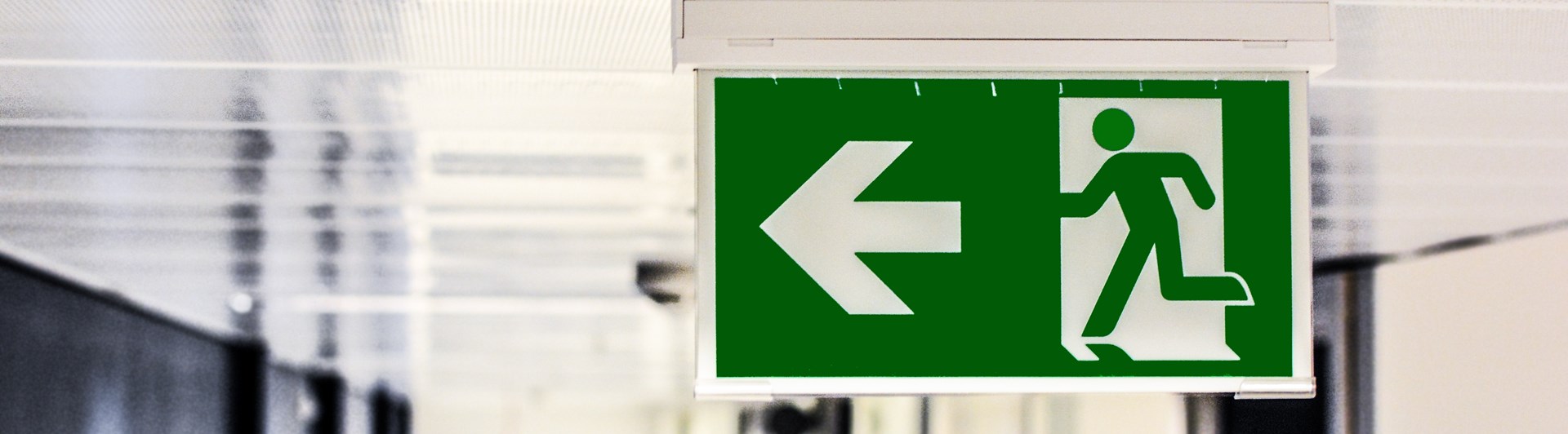 Bild på en skylt som visar en nödutgångsskylt i taket på en korridor.