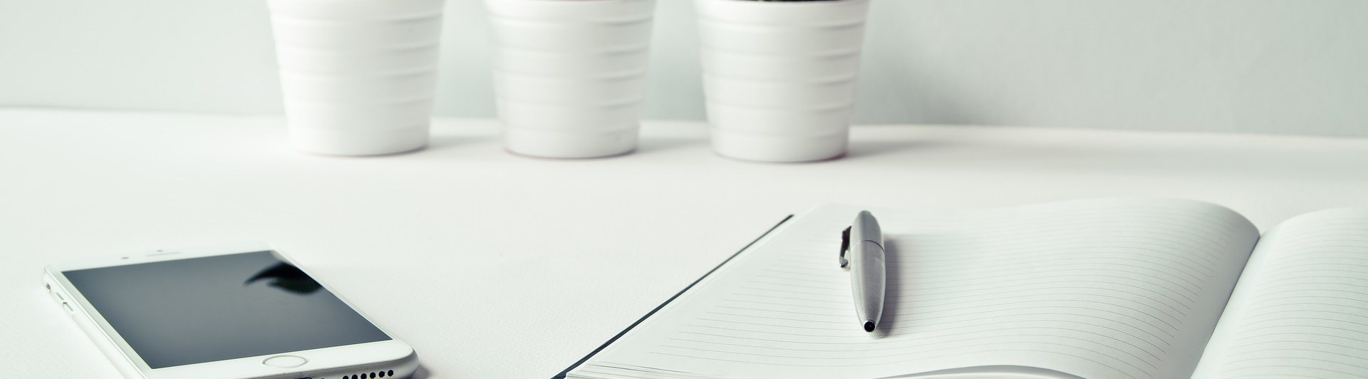 Bild som visar ett skrivbord med ett anteckningsbok, penna, mobil och tre blomkrukor.