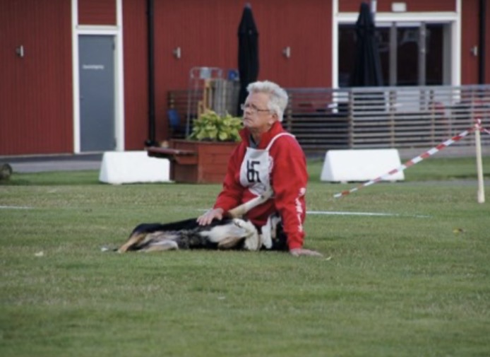 Sven sitter på gräset efter en tävling i lydnad med sin hund