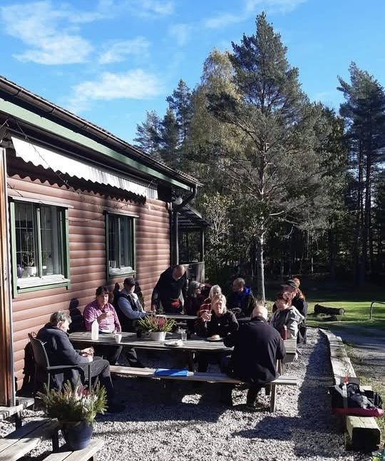 Människor sitter utomhus framför en klubbstuga 