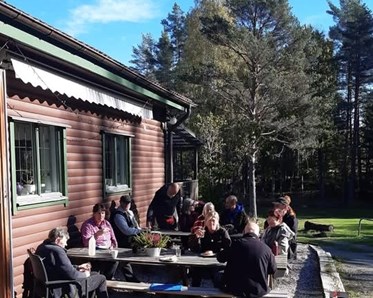 Människor sitter utomhus framför en klubbstuga