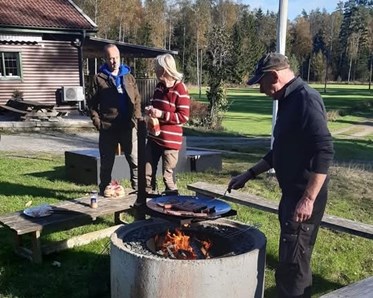 Tre människor står runt en grillplats