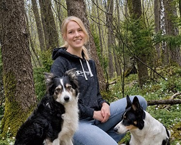 Malin Olsson sitter i skogen med sina två hundar av rasen border collie
