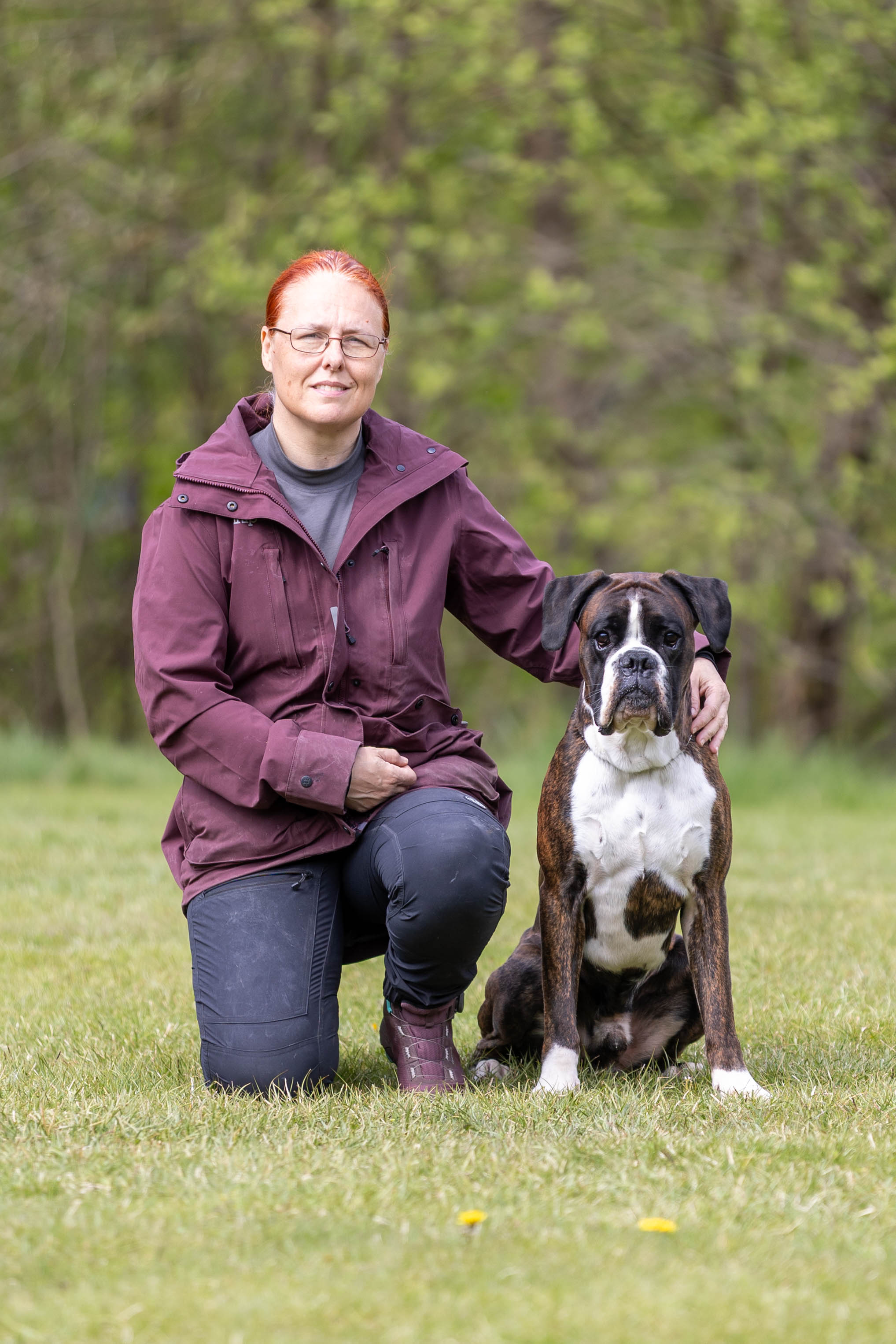 En kvinnlig hundförare som sitter bredvid sin hund som är av rasen boxer
