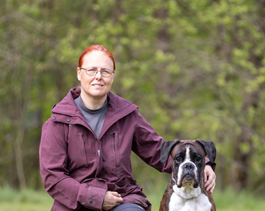 En kvinnlig hundförare som sitter bredvid sin hund som är av rasen boxer