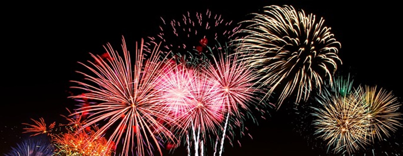 Fyverkerier på en mörk himmel i olika toner av rosa och guld.