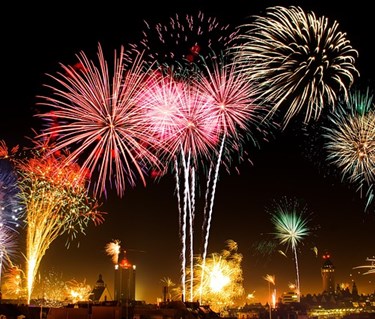 Fyverkerier på en mörk himmel i olika toner av rosa och guld.