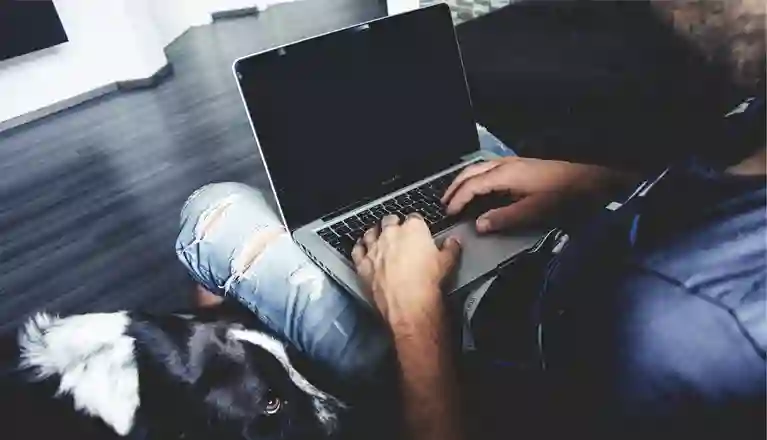 En man som sitter vid datorn med en hund bredvid sig
