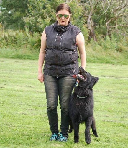 Kvinna med solglasögon tränar fot med sin hund. Hunden går på hennes vänstar sida och tittar upp på henne