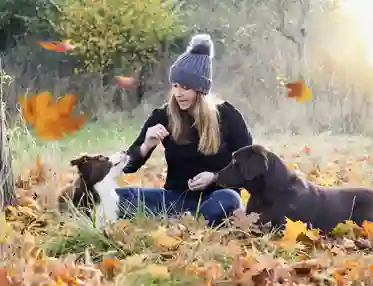 Kvinna sitter tillsammans med två hundar bland löv