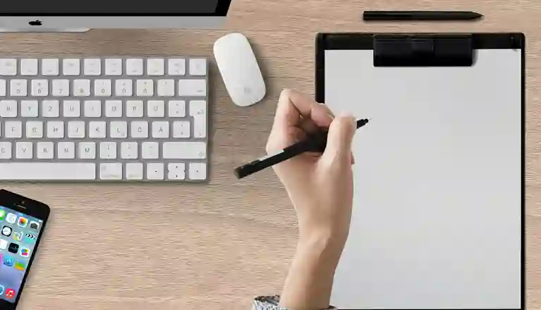 Bild som visar en skrivande hand på papper på ett skrivbord.