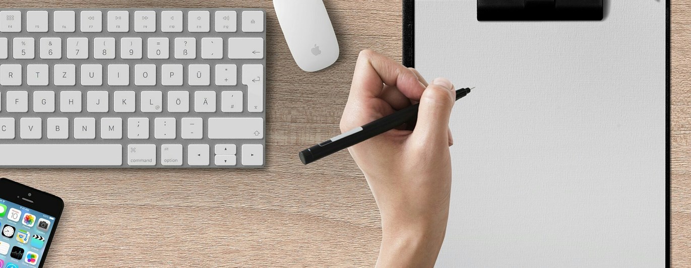 Bild som visar en skrivande hand på papper på ett skrivbord.