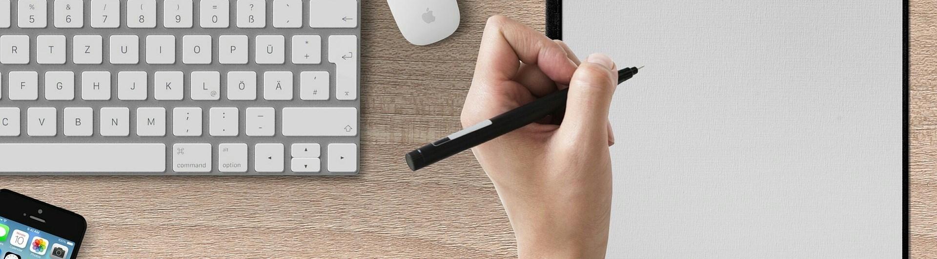 Bild som visar en skrivande hand på papper på ett skrivbord.