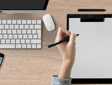 Bild som visar en skrivande hand på papper på ett skrivbord.