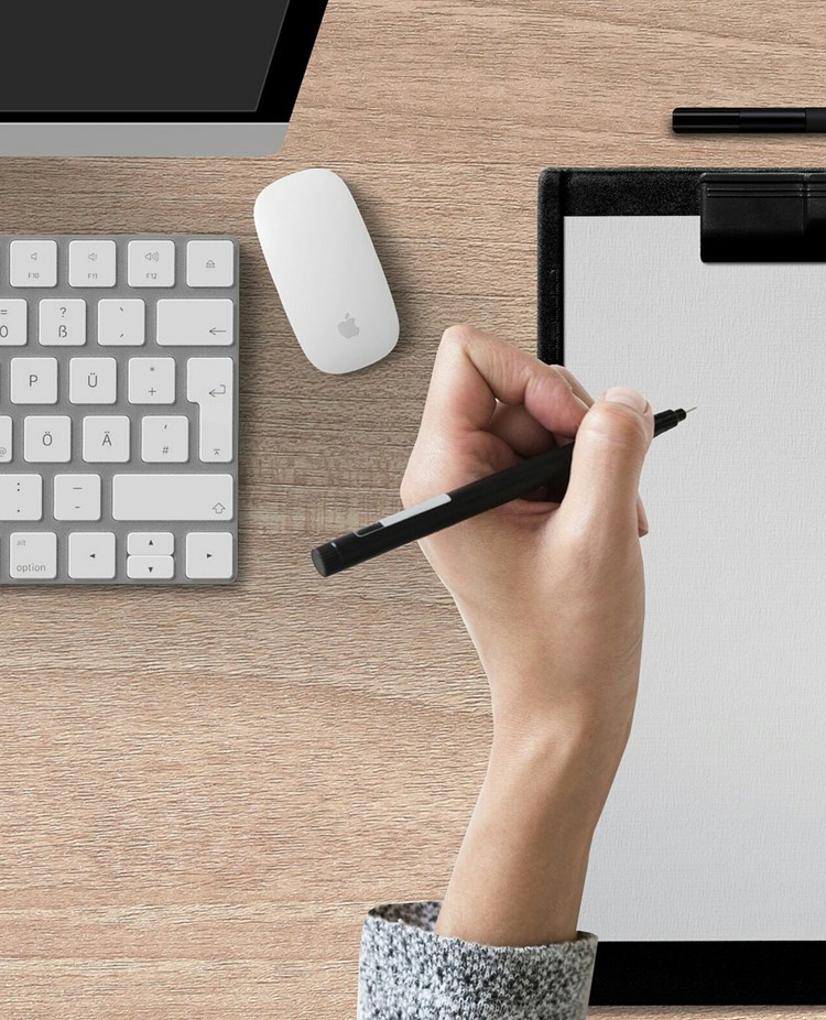 Bild som visar en skrivande hand på papper på ett skrivbord.