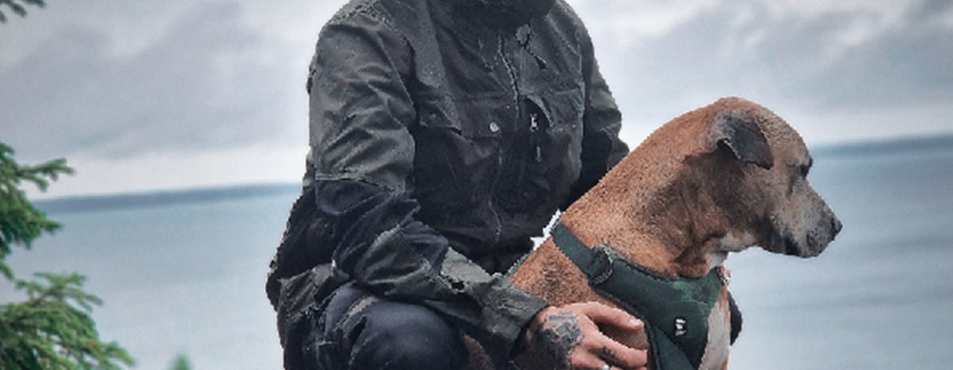 Reklambild för Arrak, man i regnponcho klappar en hund