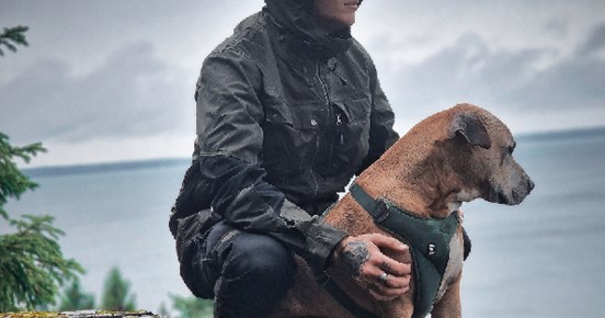 Reklambild för Arrak, man i regnponcho klappar en hund