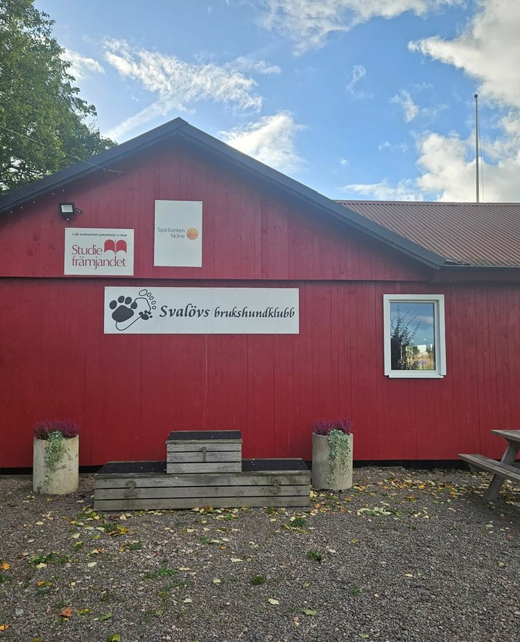 Röd klubbstuga i trä. På bilden syns också fina krukor med blommor.