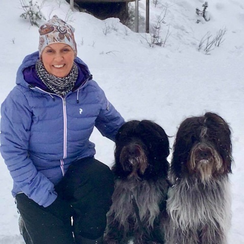 Kvinna i blå jacka som sitter bredvid två svart/vita hundar som sitter ner