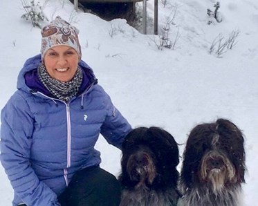 Kvinna i blå jacka som sitter bredvid två svart/vita hundar som sitter ner