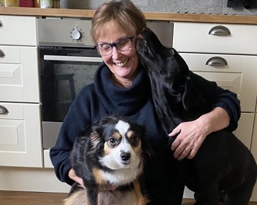 Kvinna med två hundar där den ena hunden slickar henne i ansiktet