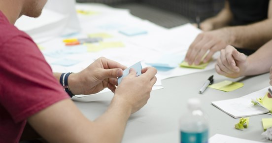 Människor som sitter vid ett bord med anteckningsböcker, pennor och post-it lappar