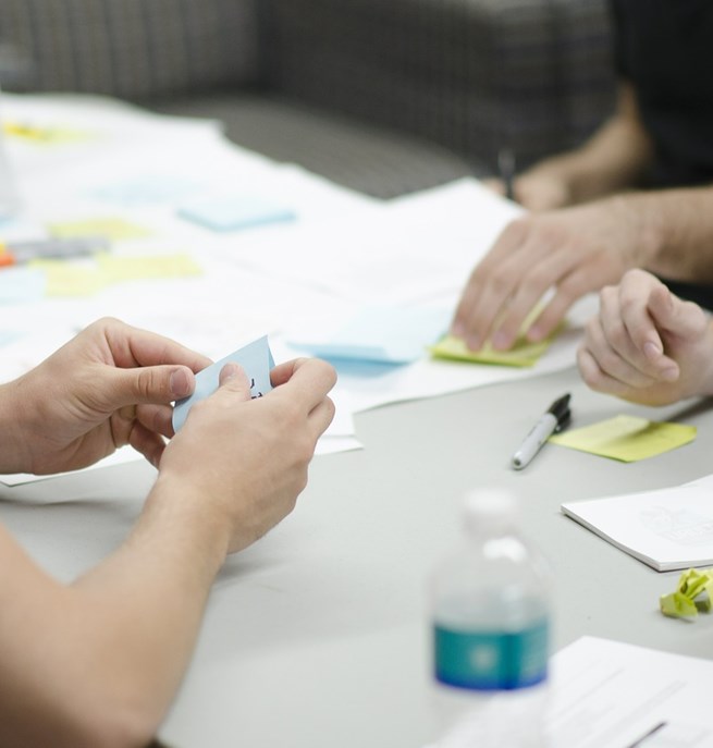 Människor som sitter vid ett bord med anteckningsböcker, pennor och post-it lappar