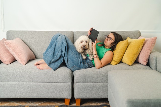 Matte med hund som ligger på soffan och läser i mobilen