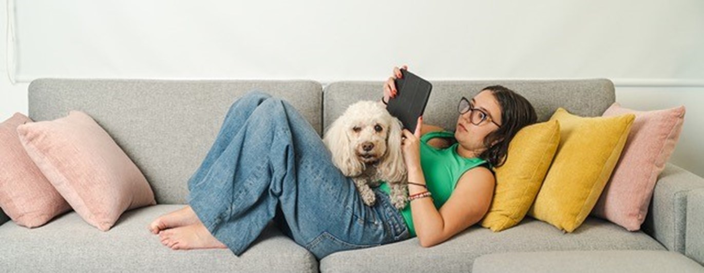 Matte med hund som ligger på soffan och läser i mobilen