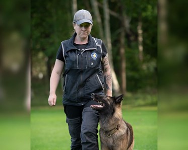 Hund som går fot bredvid sin kvinnliga förare.
