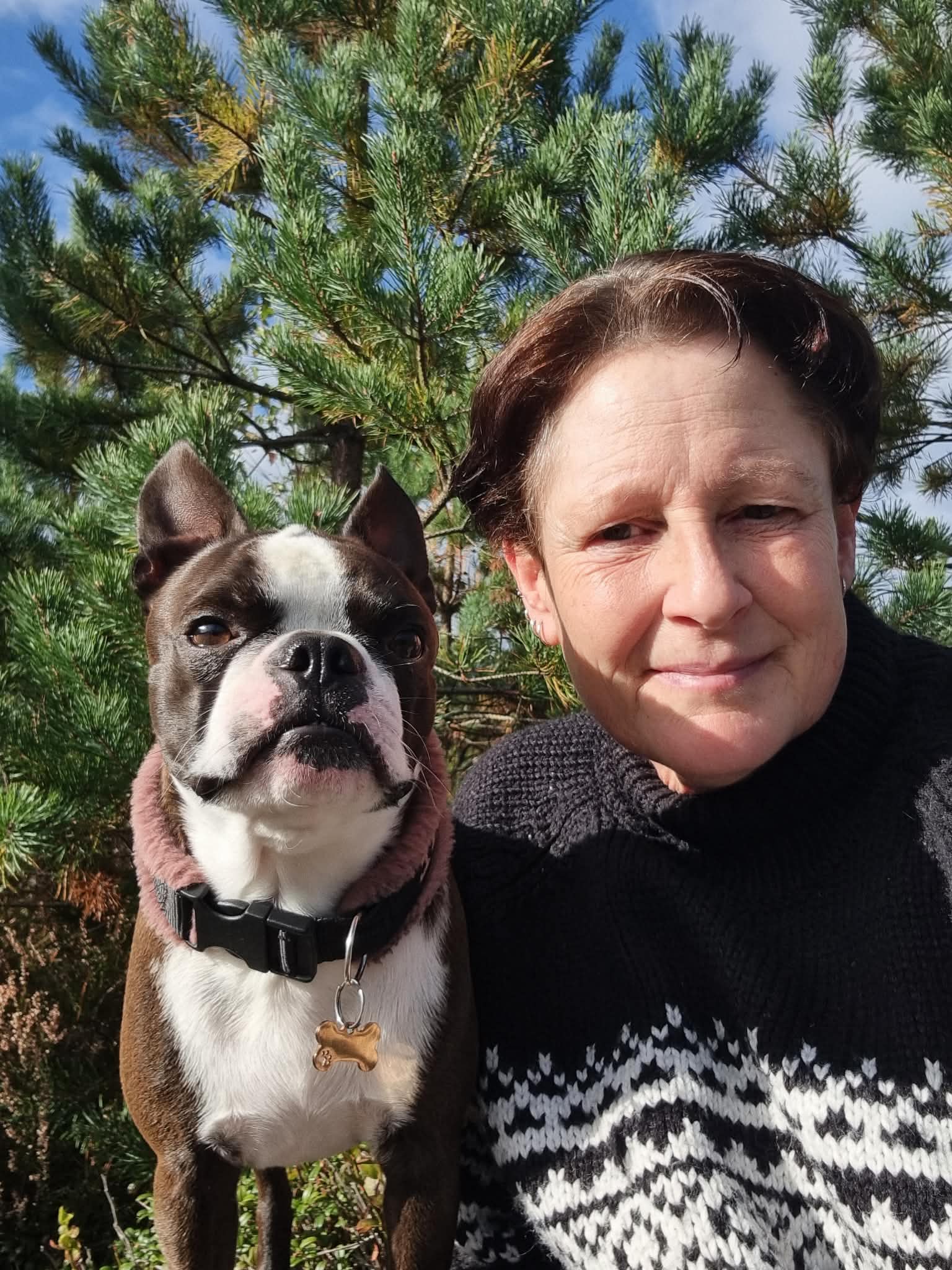 En matte kramar om sin bostonterrier och kisar mot solen.