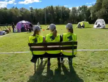 Tre tjejer sitter på en bänk med ryggen mot kameran med SBK Göteborgsavdelningens logga på ryggen på reflexvästen.